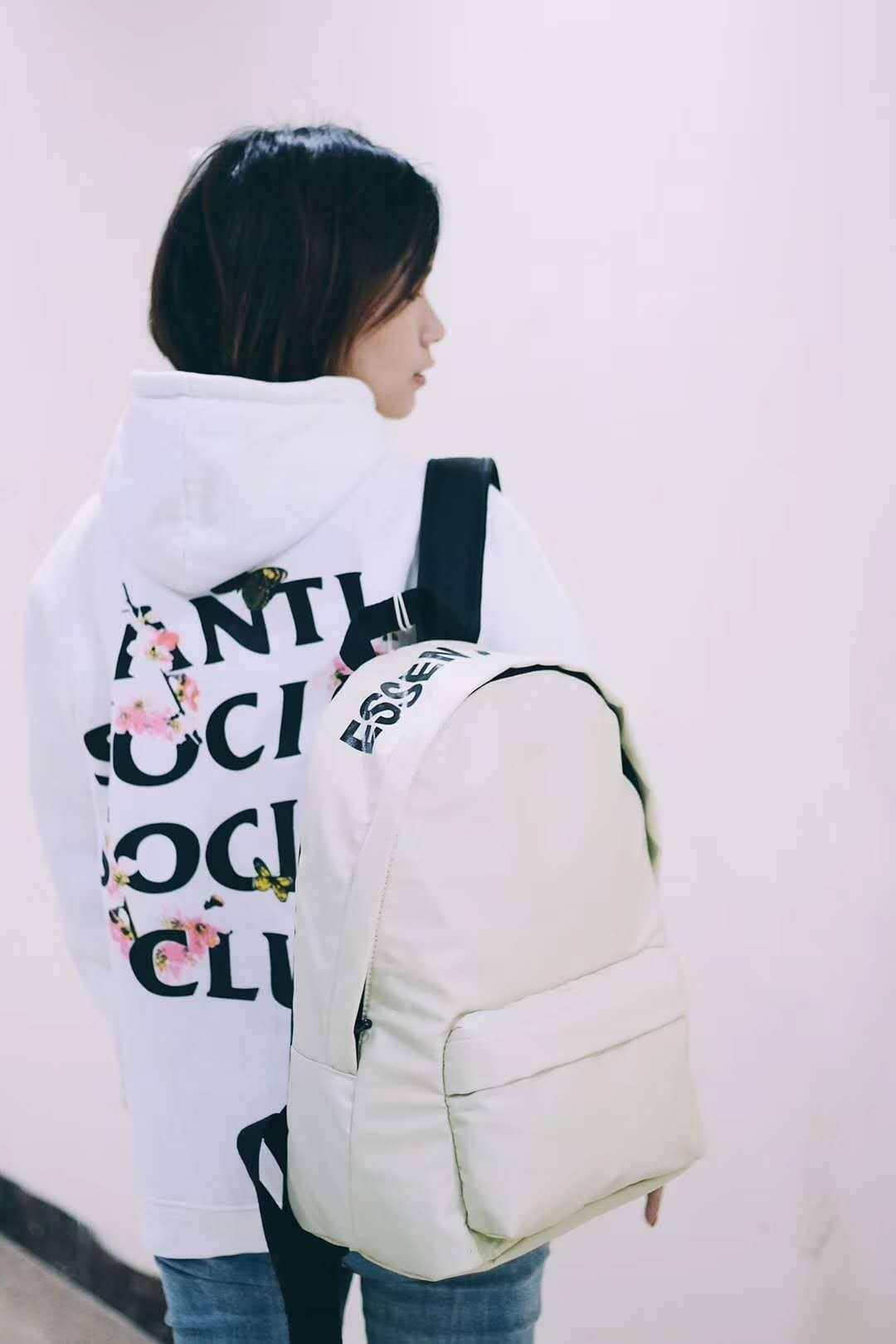 Backpack with kpop logo, female wearing hoodie with pink cherry blossoms design, casual streetwear style, minimalistic background, trendy fashion accessory for fans.