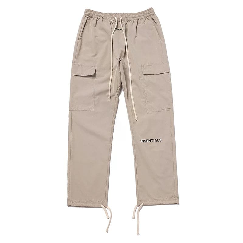 Baggy beige cargo pants with drawstrings and "ESSENTIALS" text print, streetwear style.