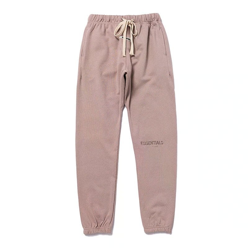 Comfy pink jogger pants with drawstring waist and "ESSENTIALS" embroidered on the thigh, perfect for casual streetwear and loungewear.