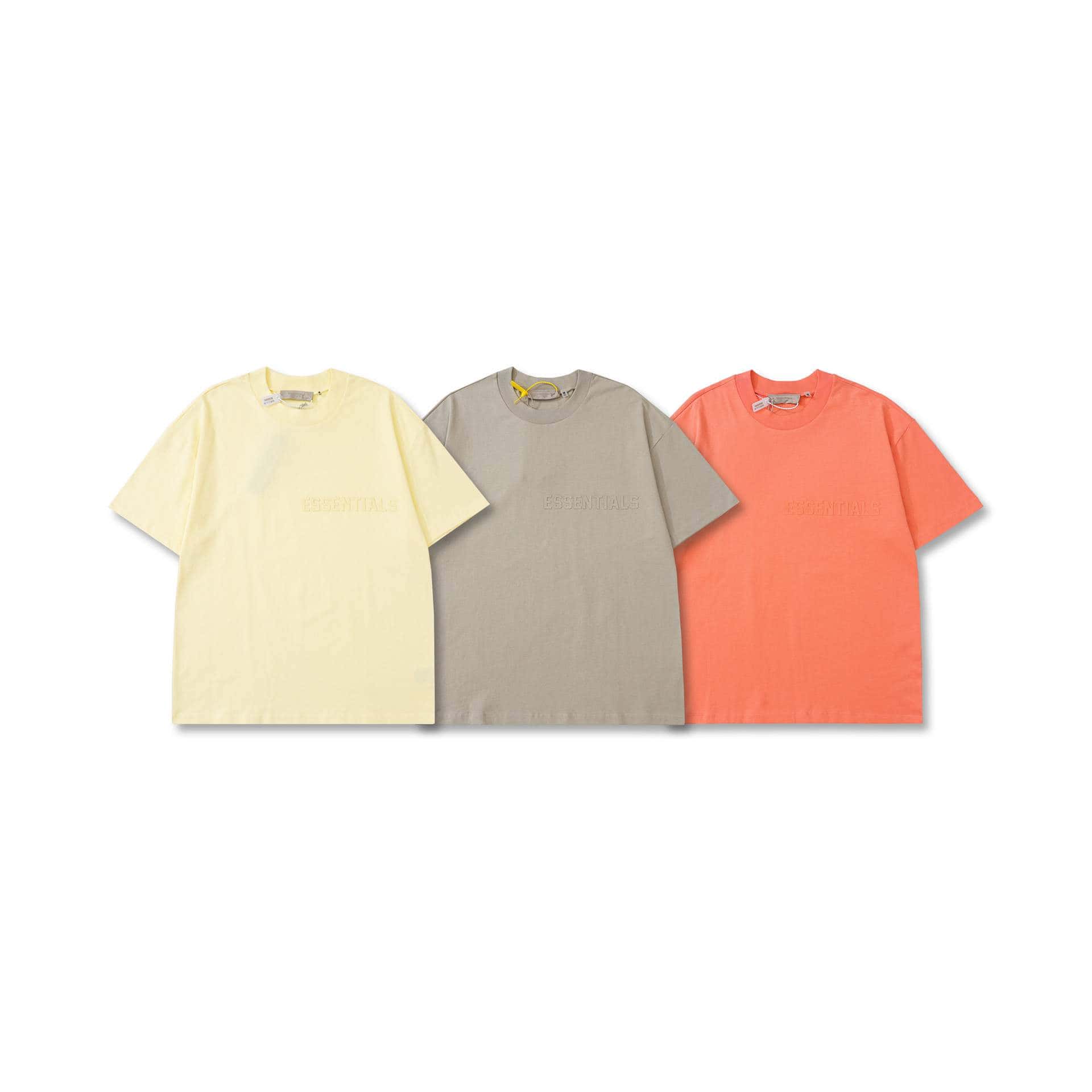 Soft pastel 2x kpop merchandise t-shirts in yellow, beige, and coral, featuring minimalist designs and "ESSENTIALS" embossed text, perfect for K-pop fans and fashion enthusiasts.