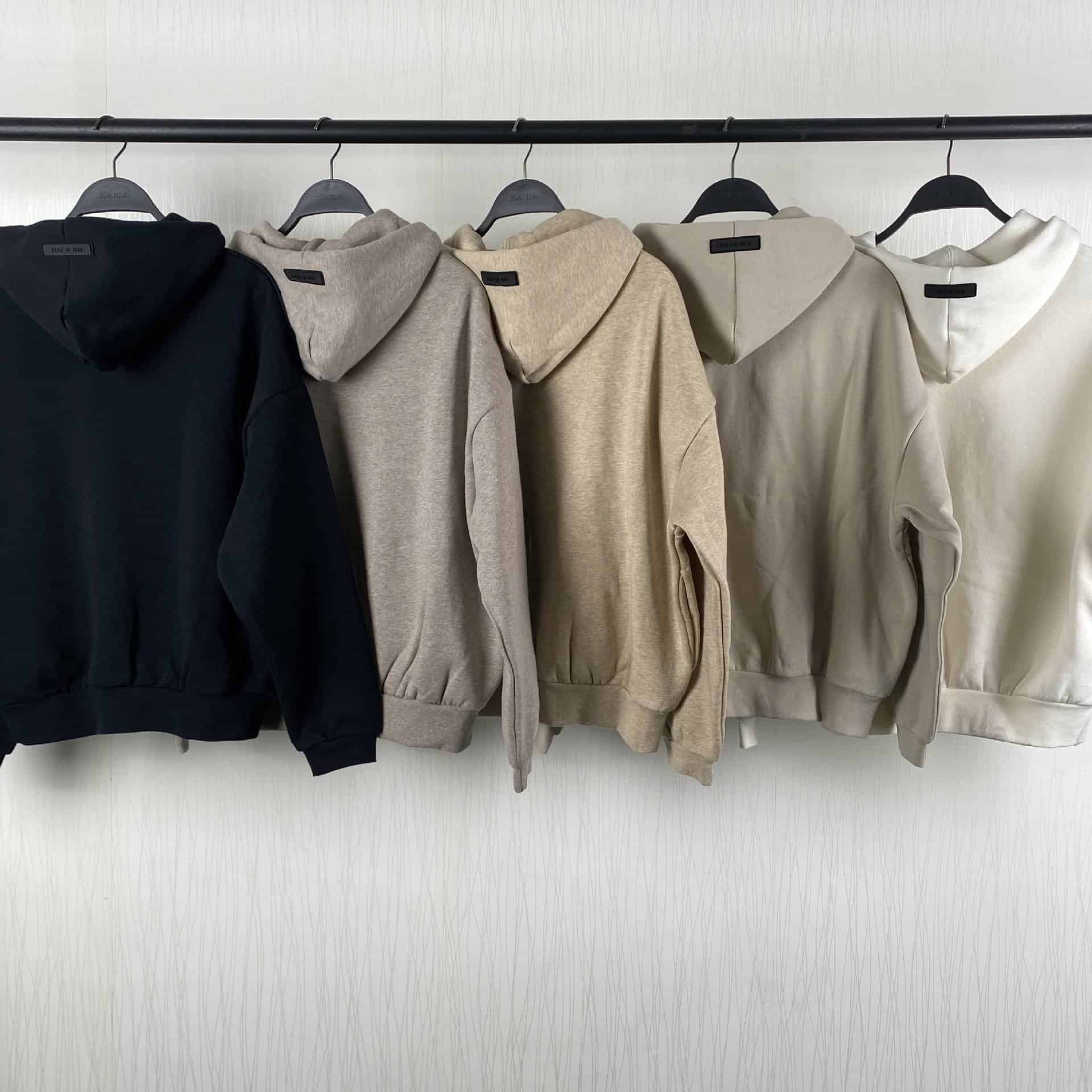 Hoodie sweatshirt with double Kpop merch logo in black, beige, and cream colors, hanging on black hangers in a row.